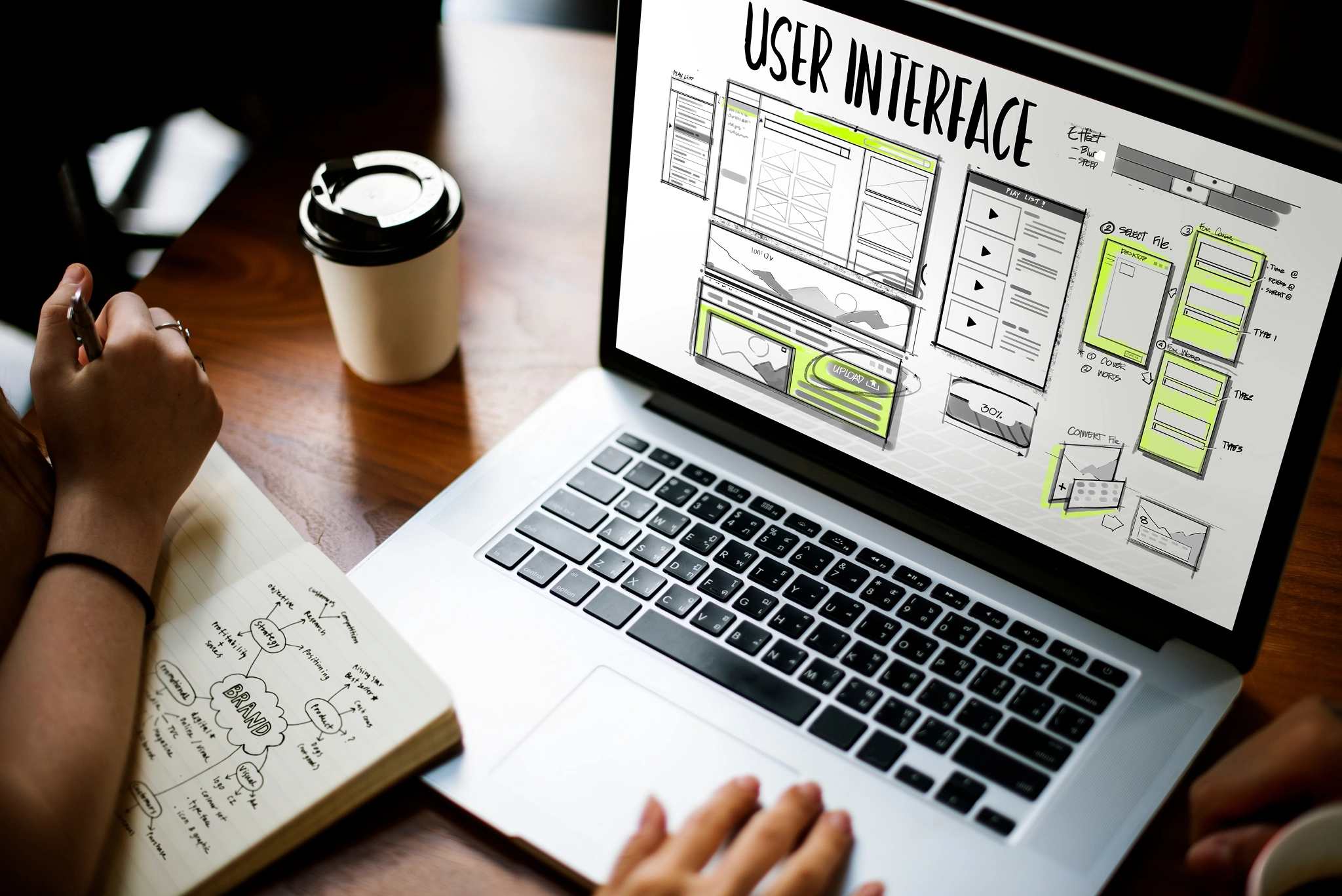 A laptop showing user interface layouts beside a notebook of design notes
